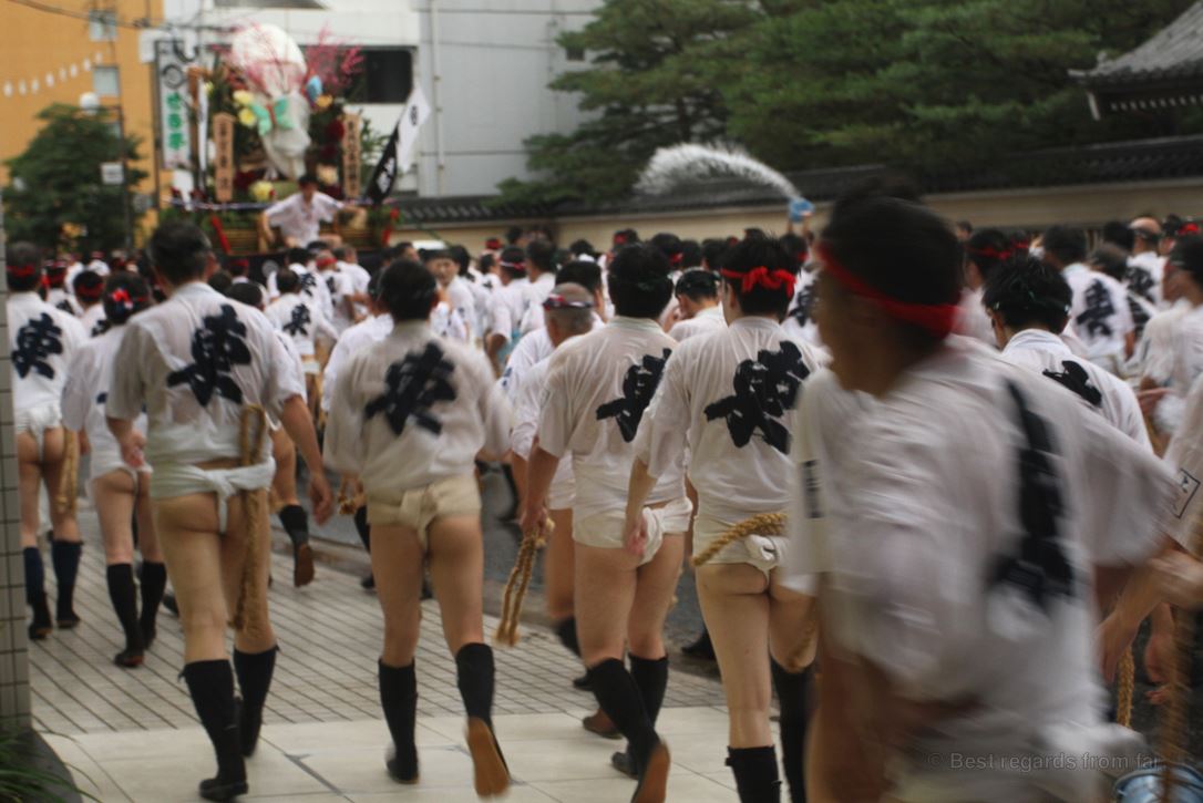 A group of Japanese men wearing the traditional outfit walks in the street behind a large float during the festival in Fukuoka, Kyushu