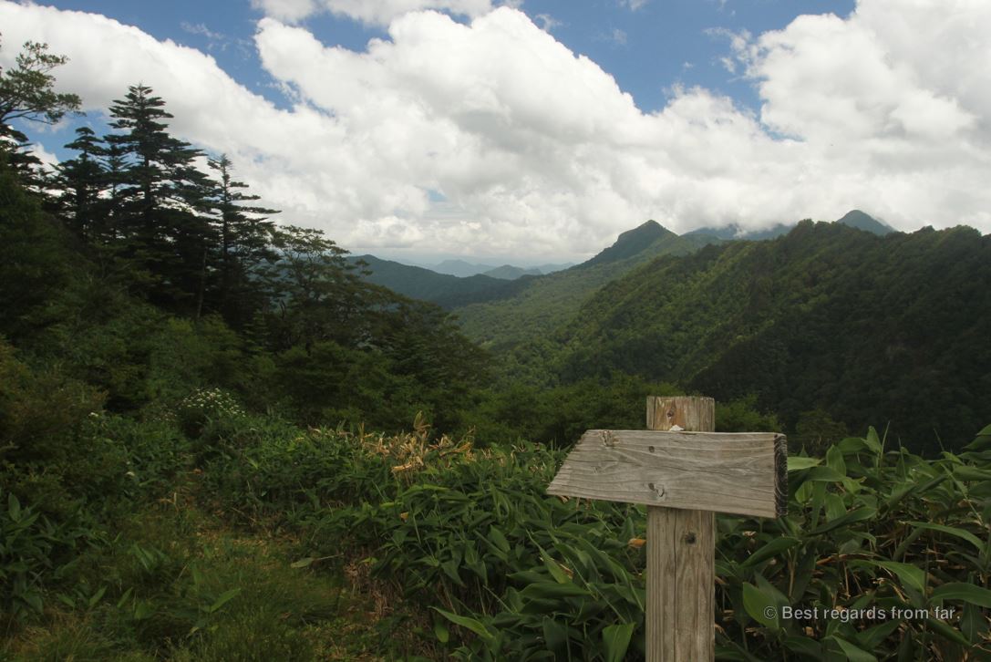 Woodedn arrow on a hiking trail in the middle of the green forest and mountains on a semi-cloudy day in Japan.