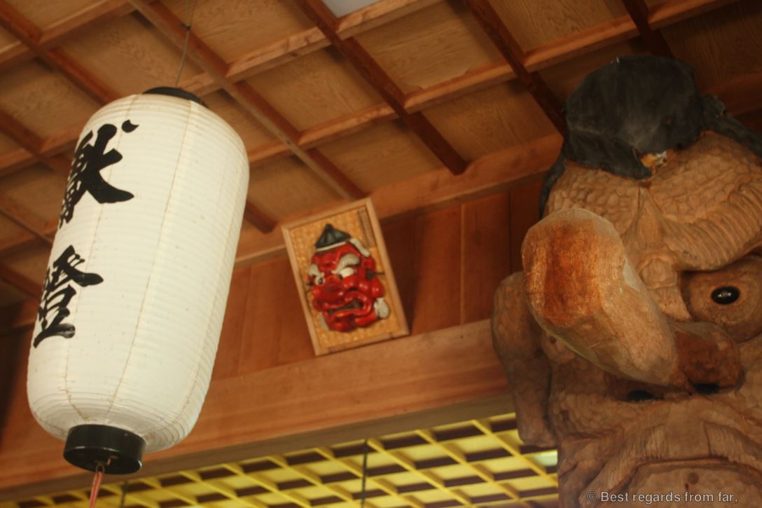 Woodcarved head with a big nose, white lantern with black Japanese letters in a shrine.