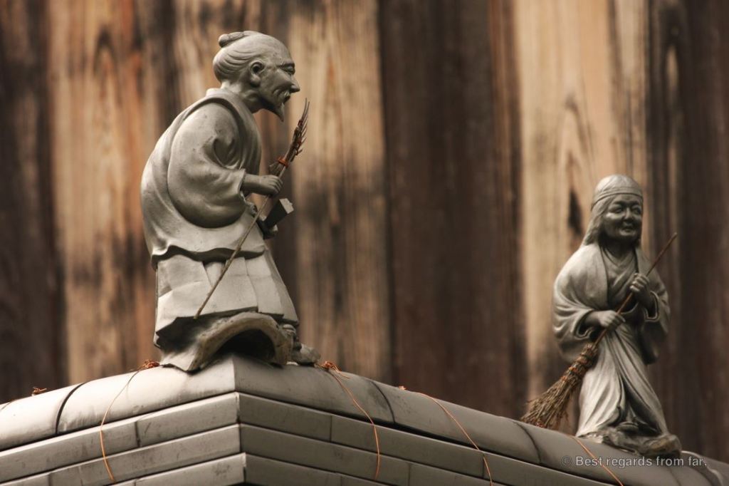 Two delicate statues along the path of philosophy, Kyoto, Japan. An old man with a broom, and his wife also carrying a broom.
