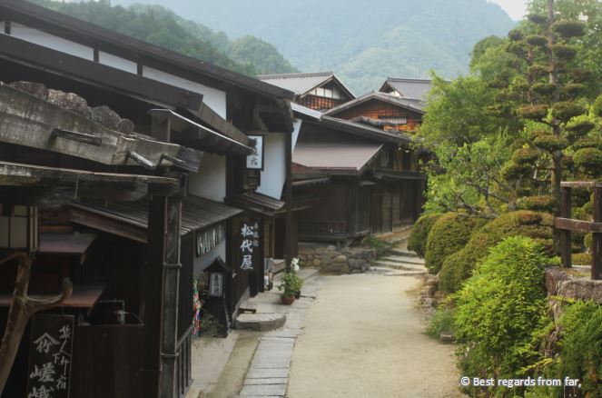 Barren street of Tsumago, white and black signboards with Japanese charcaters, trees.