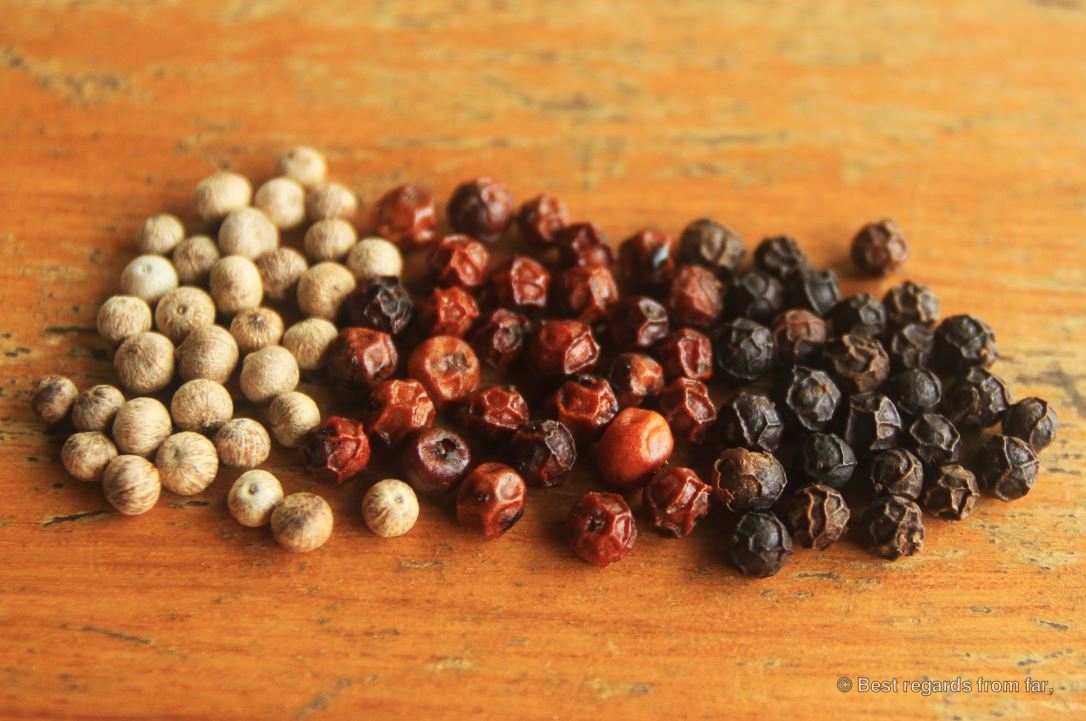 White red and black pepper on a wooden table.