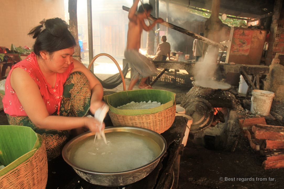Woman making rice noodles in a smoky shop.
