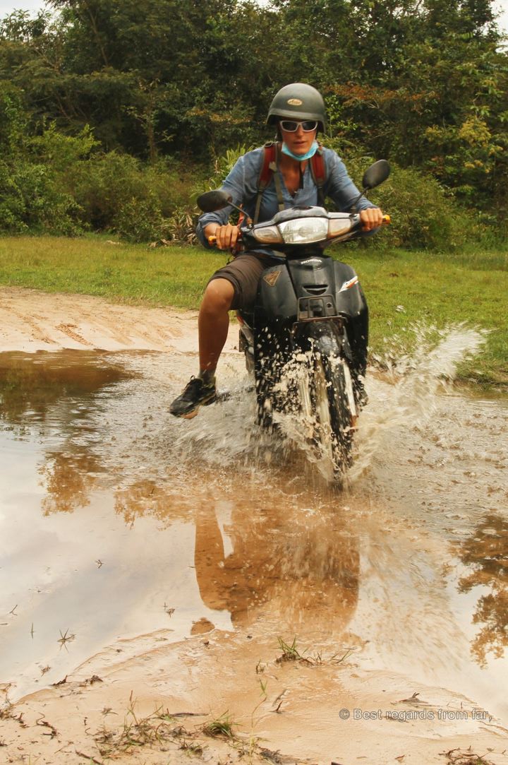 Man on a motorbike crossing a large puddle.