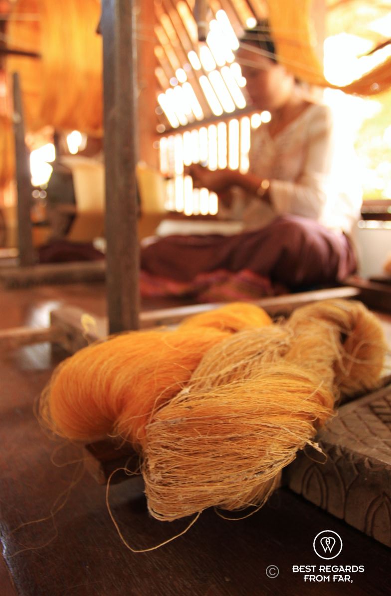 Coarse golden silk with a woman spinning behind it.