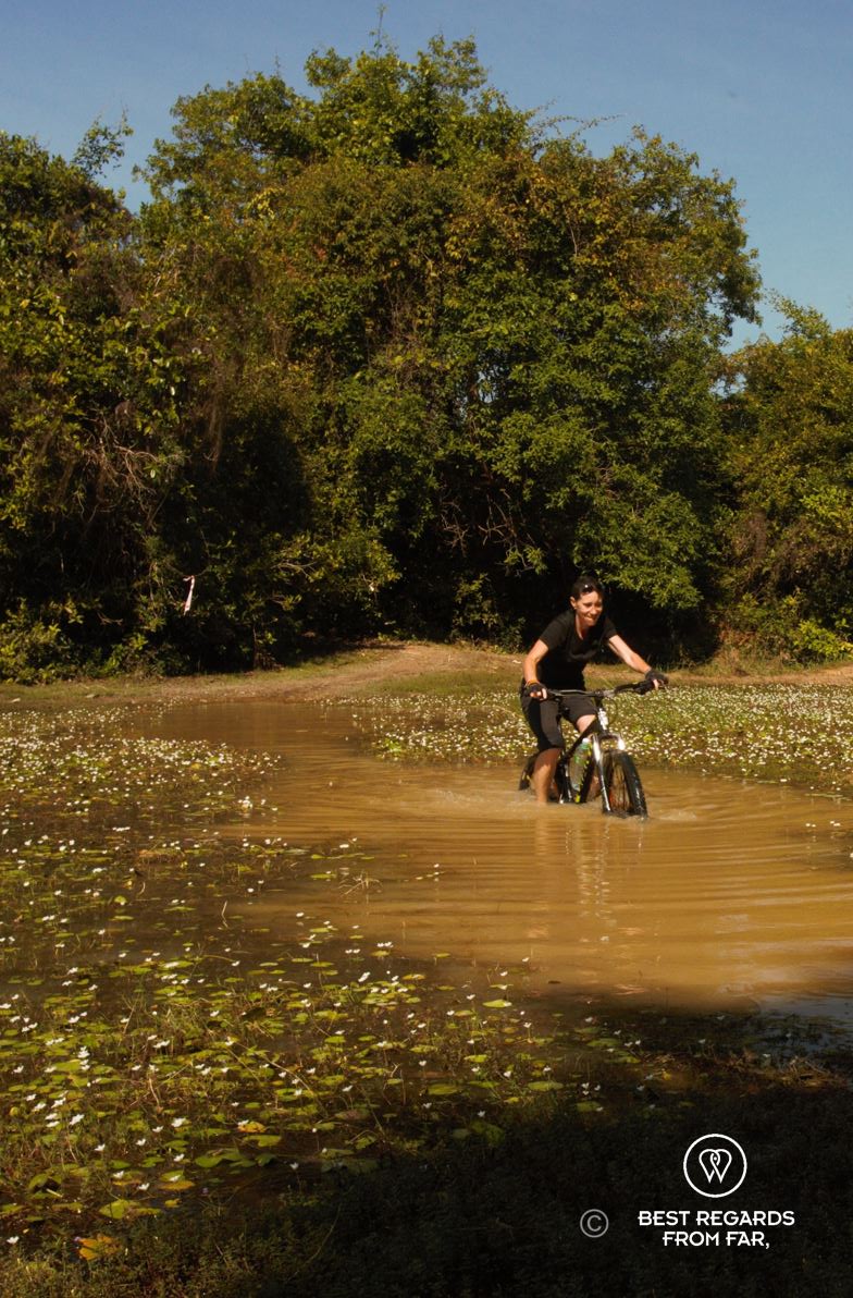 Woman biking through a large and deep puddle.