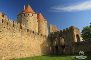 Medieval towers of Carcassonne with red roofs and the entrance gate to the castle over a moat filled with grass.