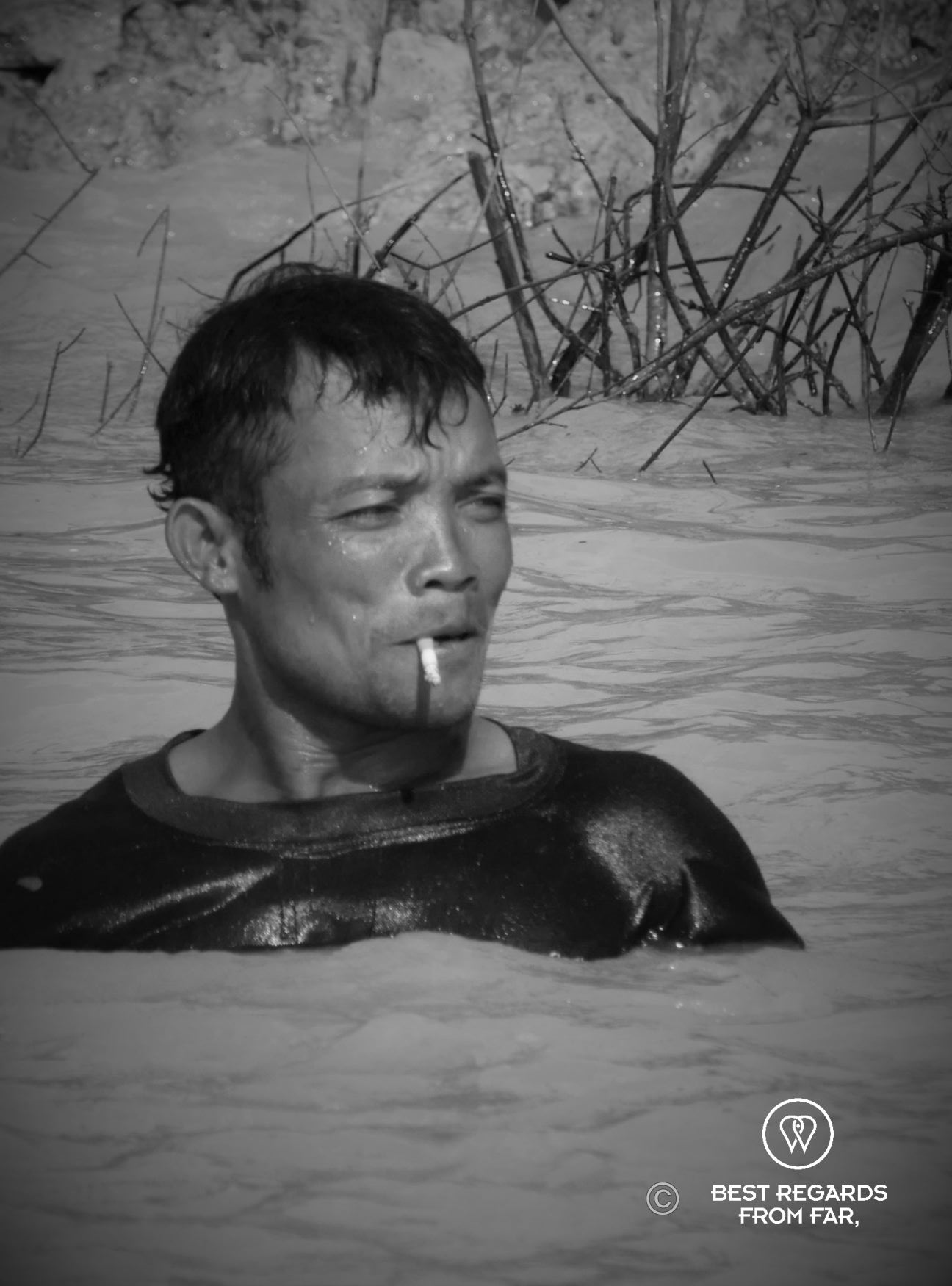 Fisherman smoking a cigarette in the river with water up to his shoulders.