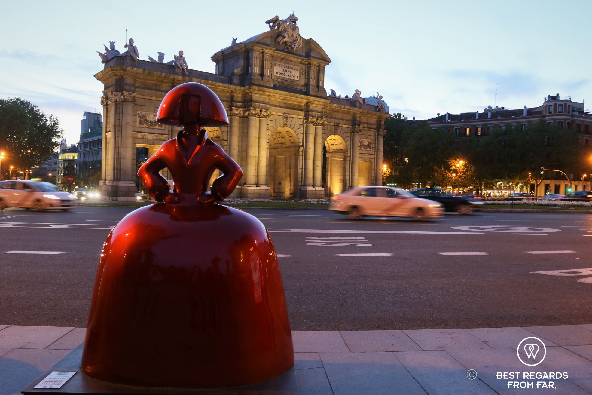 Red real-size muneca or doll in Madrid during the blue hour with cards passing by.