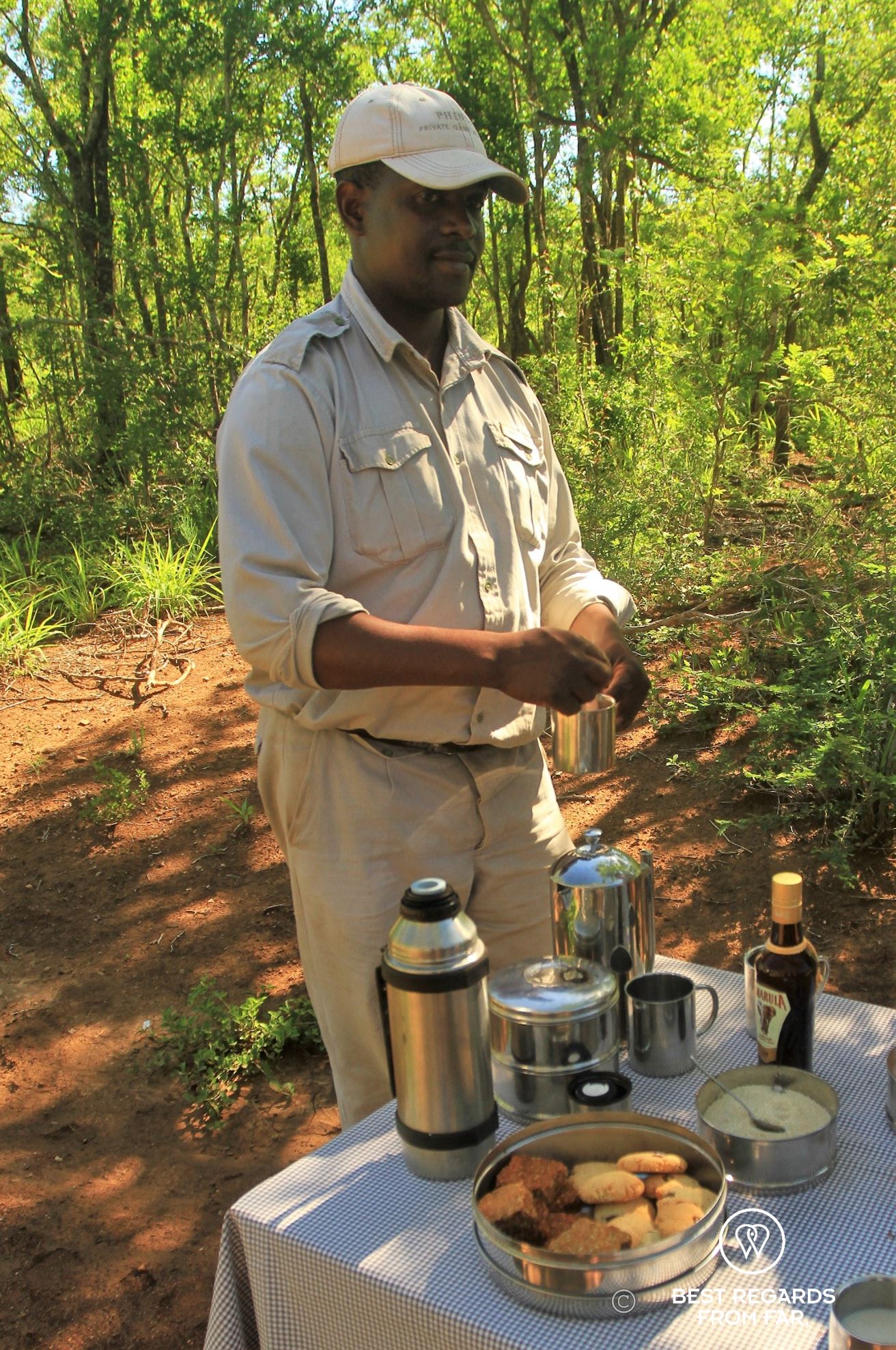 Ranger in khaki uniform and cap preparing drinks at a table with cookies in the bush.