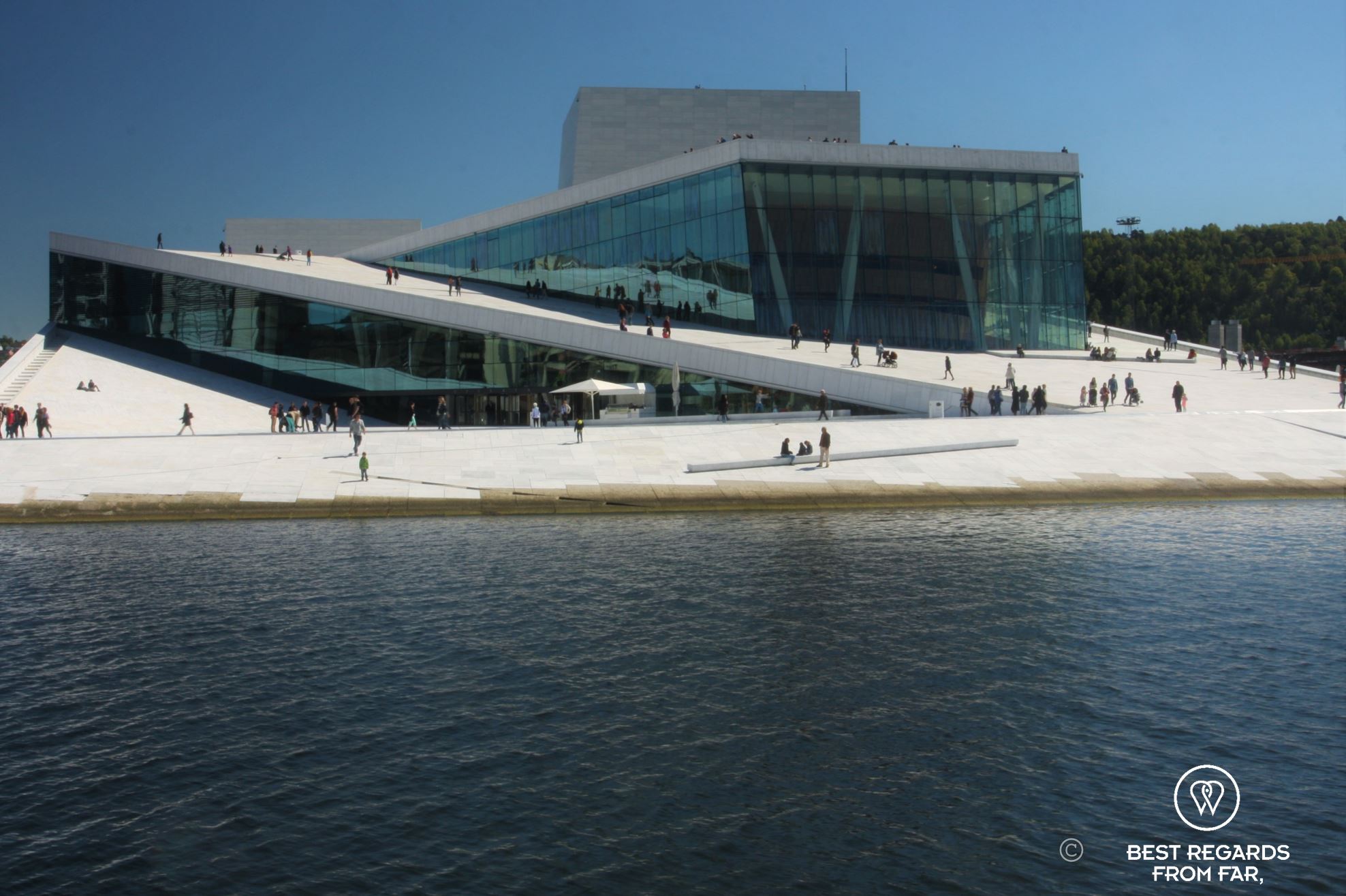 Modern building of the Oslo Opera House, white marble rising out of the water with people walking on its roof.