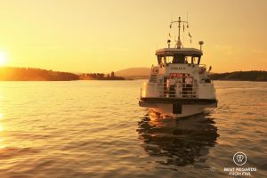 White ferry boat with two people on board on a body of water at sunset.