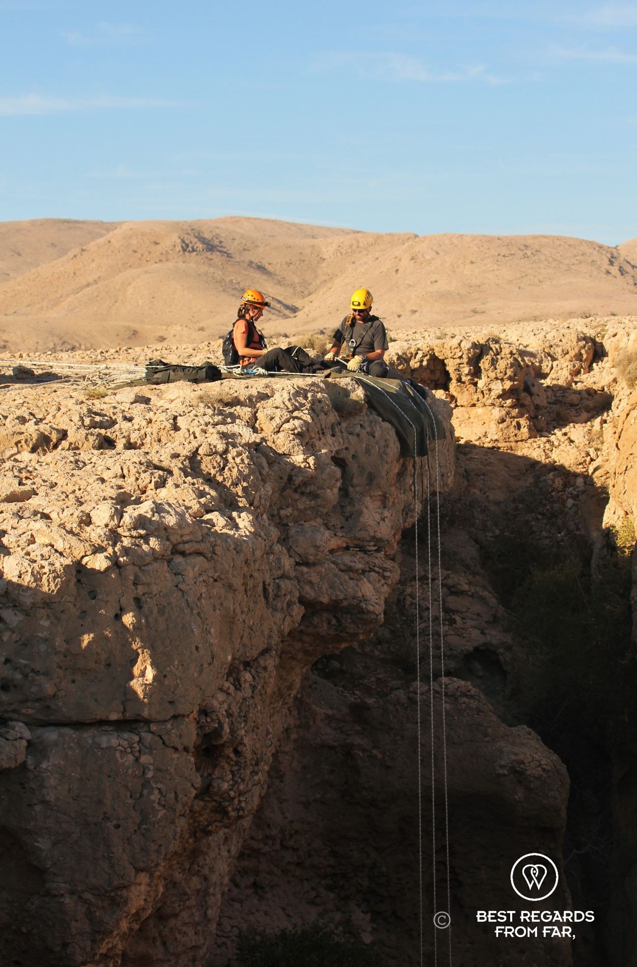Woman in full caving gear about to free abseil down a rope to explore the Seventh Hole Cave in Oman. The expert guide Justin Hall is giving her instructions.