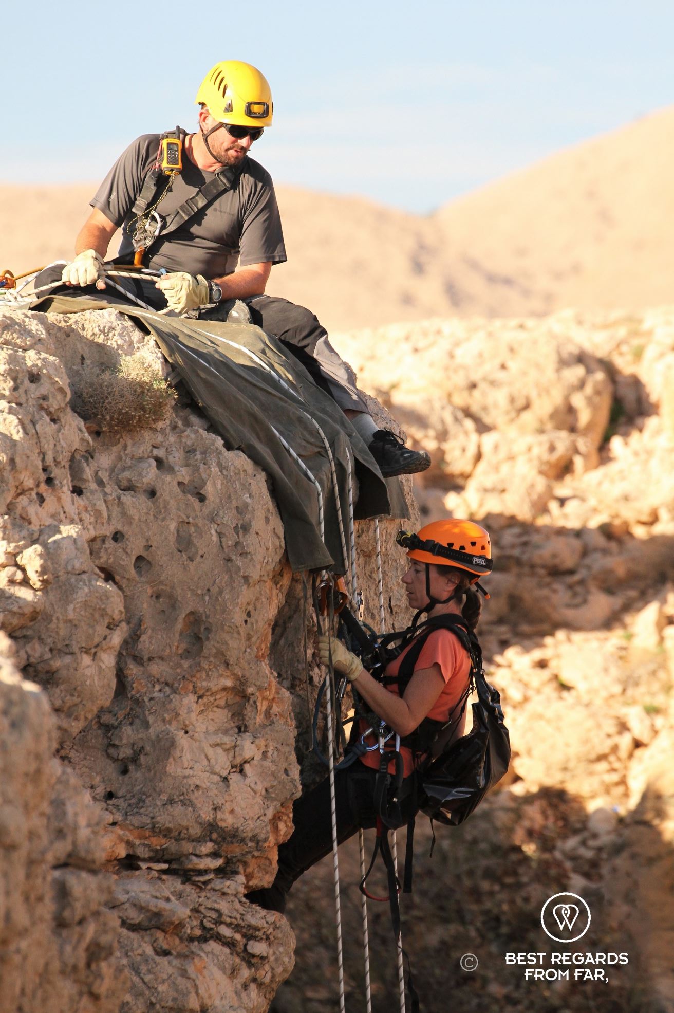 Woman in full caving gear about to free abseil down a rope to explore the Seventh Hole Cave in Oman. The expert guide Justin Hall is giving her instructions.