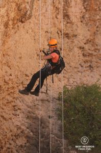 Woman in full caving gear free abseiling down a rope to explore the Seventh Hole Cave in Oman.
