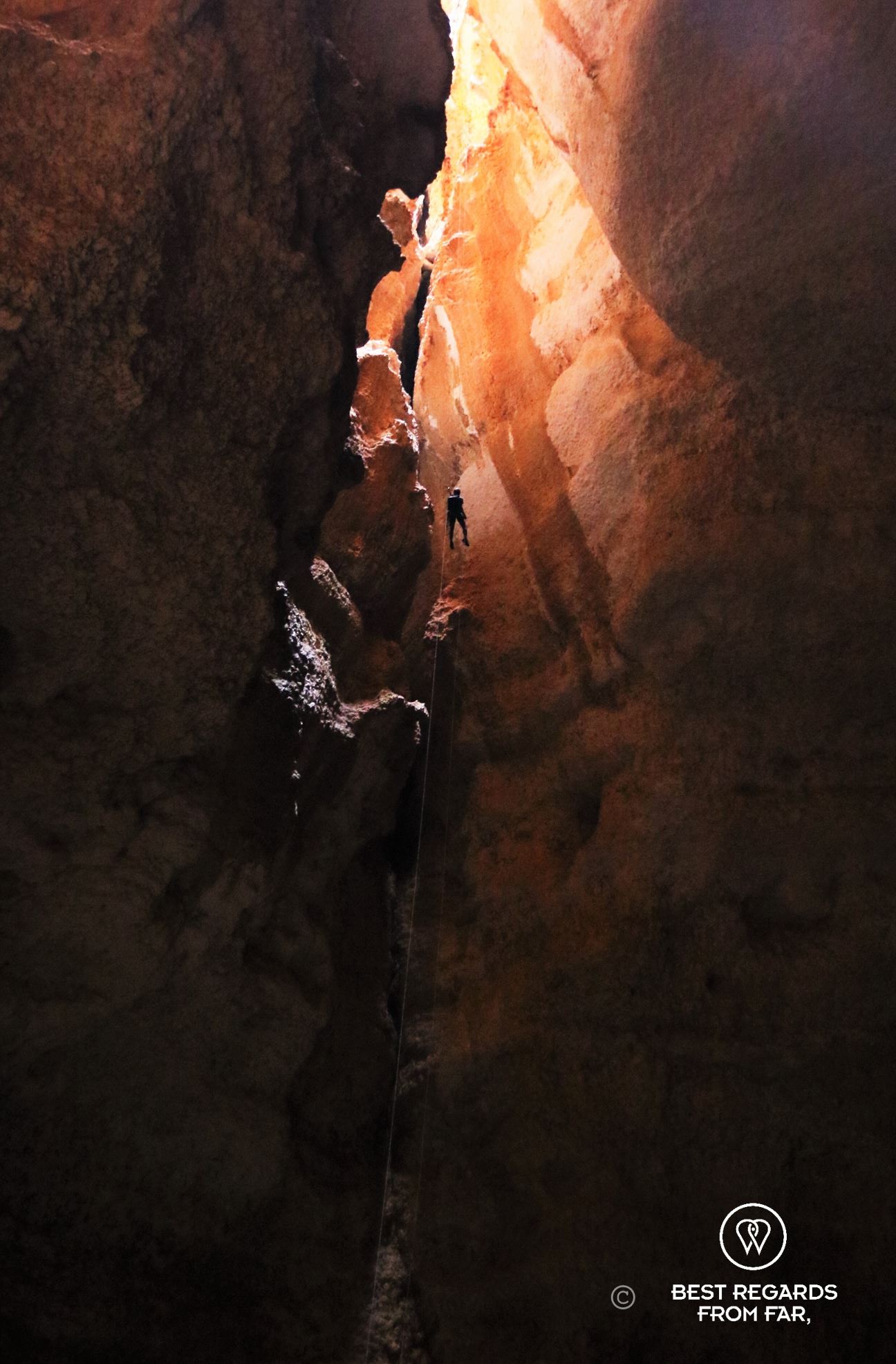 One person free abseiling down a rope to explore the Seventh Hole Cave in Oman. The abseil is so long (120 meters) that the caver looks tiny among the rocks.