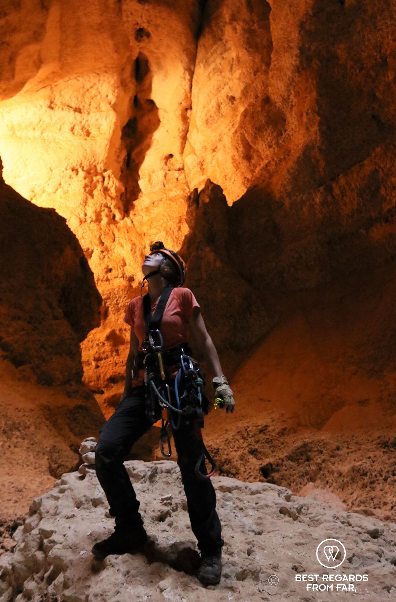 A woman in full technical caving gears looking up from the bottom of the Seventh Hole Cave in Oman.