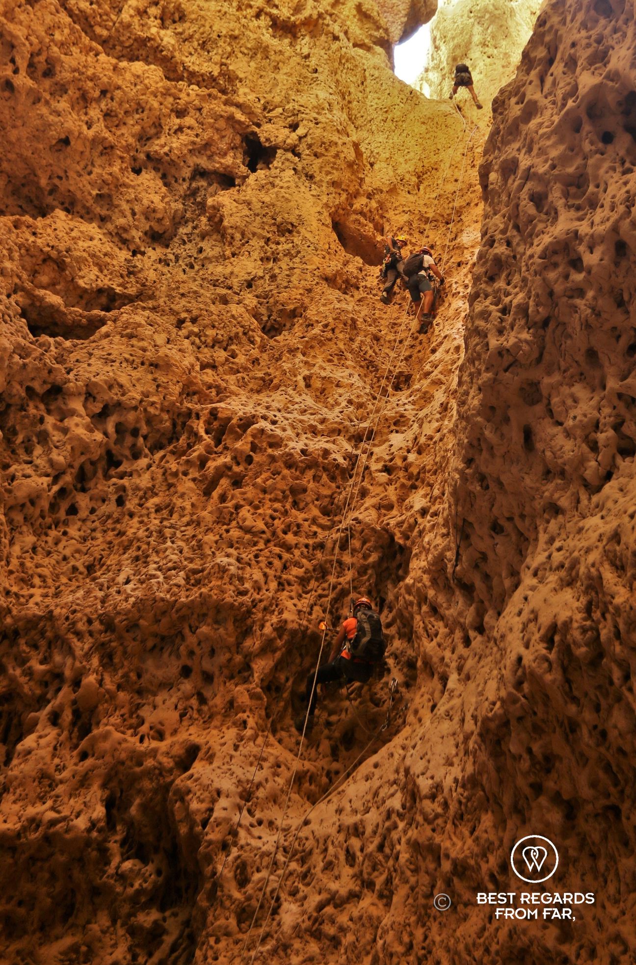 Several people climbing up along rocks on different rope sections from the bottom of the Seventh Hole Cave in Oman.