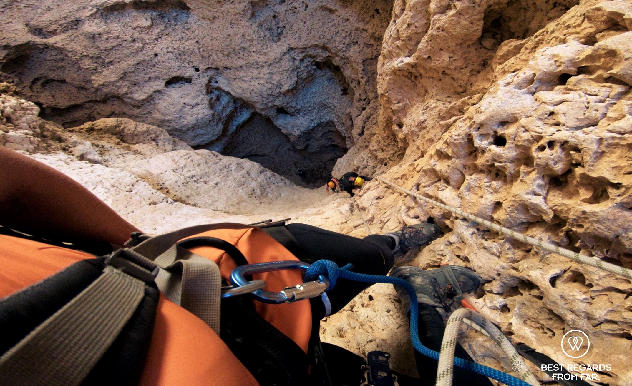 Caver on ropes in gull technical gear looking down: two other cavers are climbing back up from the Seventh Hole Cave in Oman.