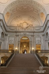 Groom and bride in on the top of a staircase in a city hall.
