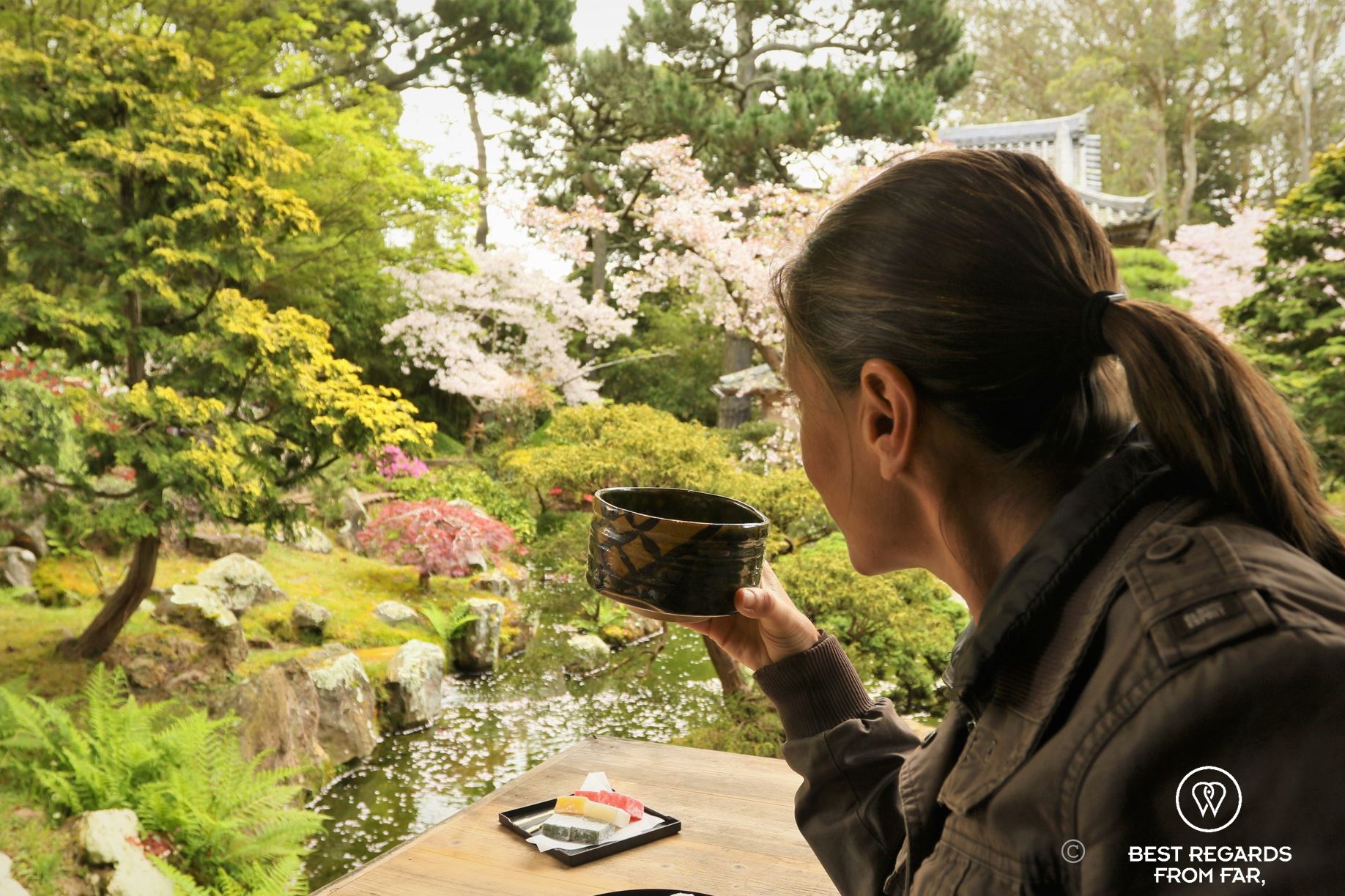 Author Claire Lessiau holding a ceramic cup with green tea while watching cherry blossoms.