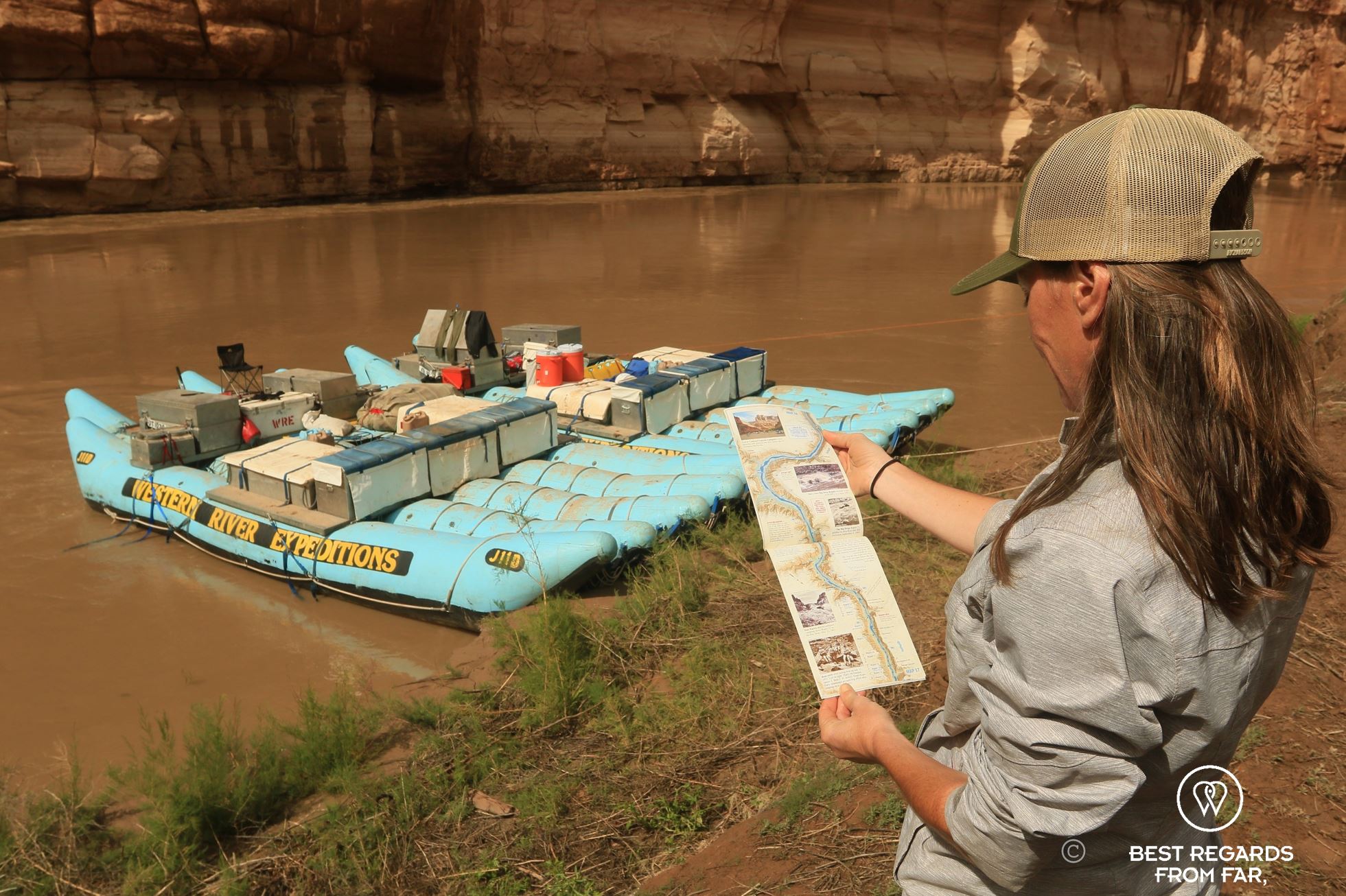 Photographer Claire Lessiau studying the rafting map of the Cataract Canyon on the bank of the Colorado River, with the rafts in the background, Western River Expeditions, USA.