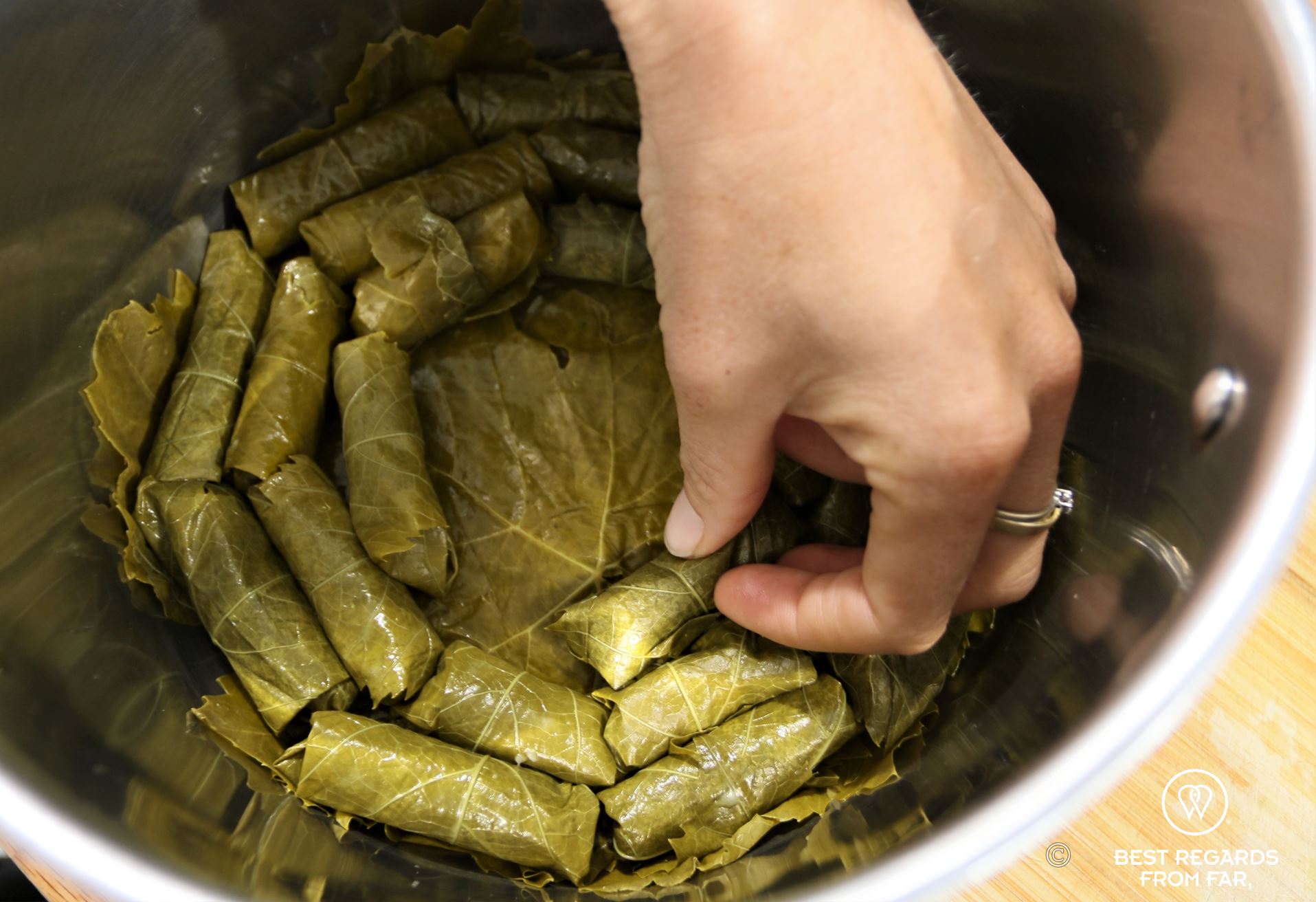 Silver pan with a hand placing green dolmades in a circle.