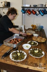 Woman wearing black preparing Greek food in a kitchen.