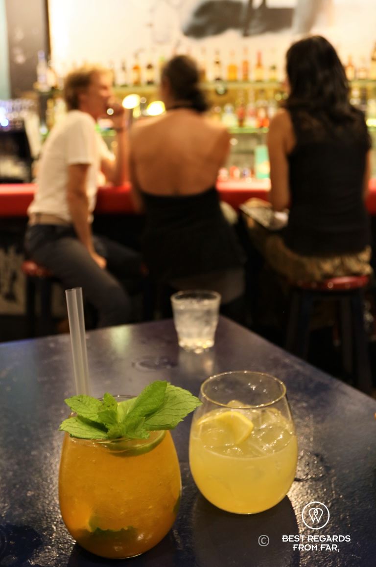 Cockatails on a table and three people sitting at a bar.