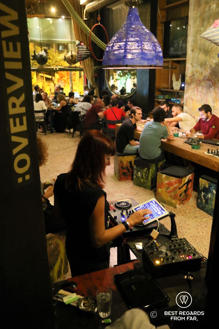 DJ making music in a bar where people are seated on long tables.