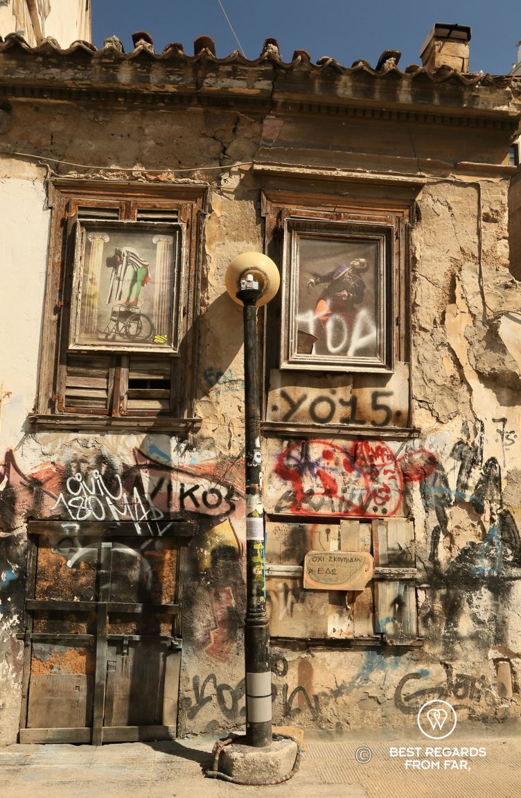 Wall with graffiti, two windows replaces by paintins and a broken lamp. Psiri, Athens, Greece.