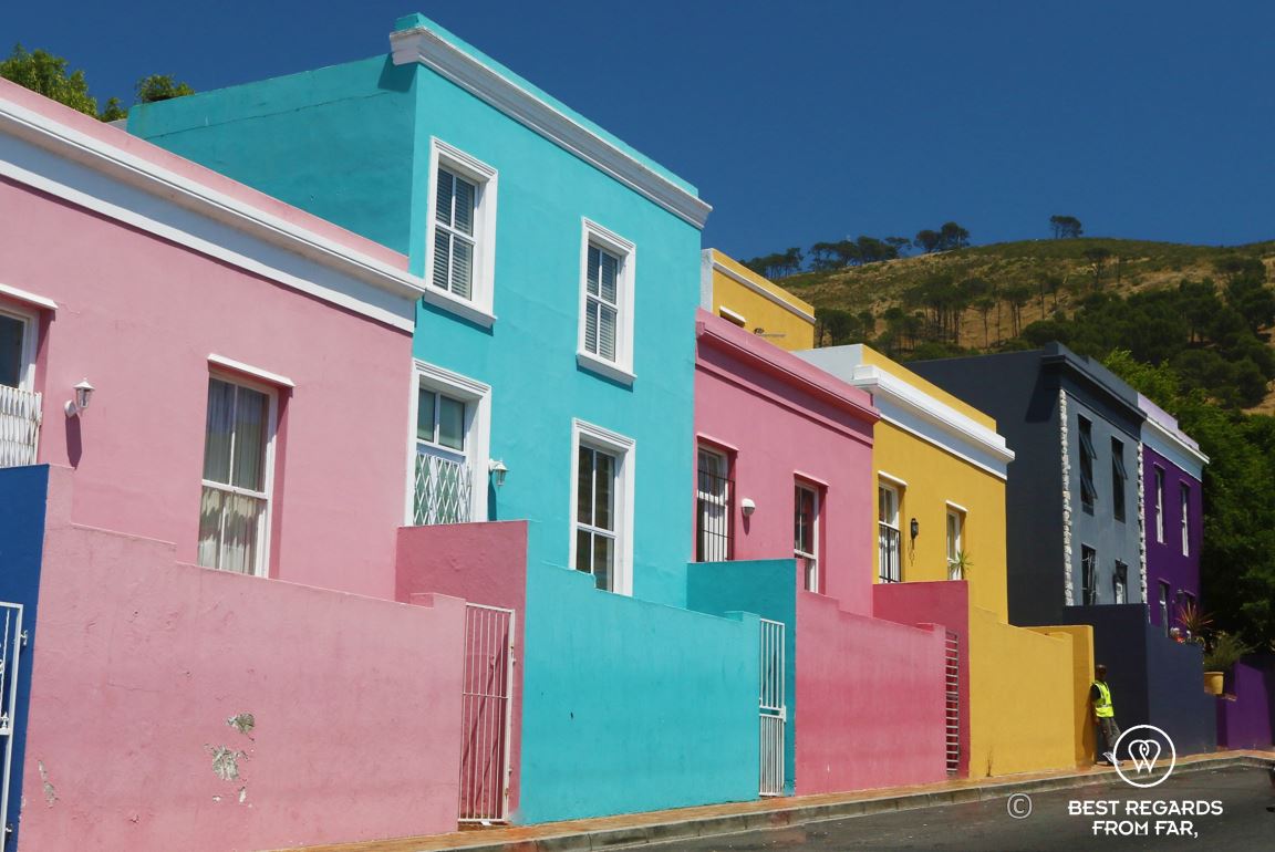 Row of colourful houses, pink, blue, yellow and purple, contrasting with Signal Hill and blue skies in Bo Kaap, Cape Town.