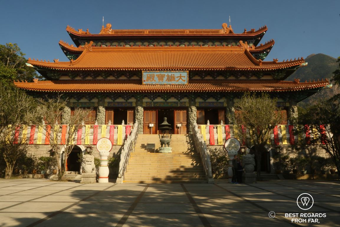 Po Lin monastery, orange roof in three layers, Chinese symbols above staircase, Lantau Island, Hong Kong.