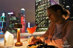 Female guest having a cocktail in a stylish bird glass at the Popinjays rooftop bar at night, the Murray Hotel, Hong Kong Island