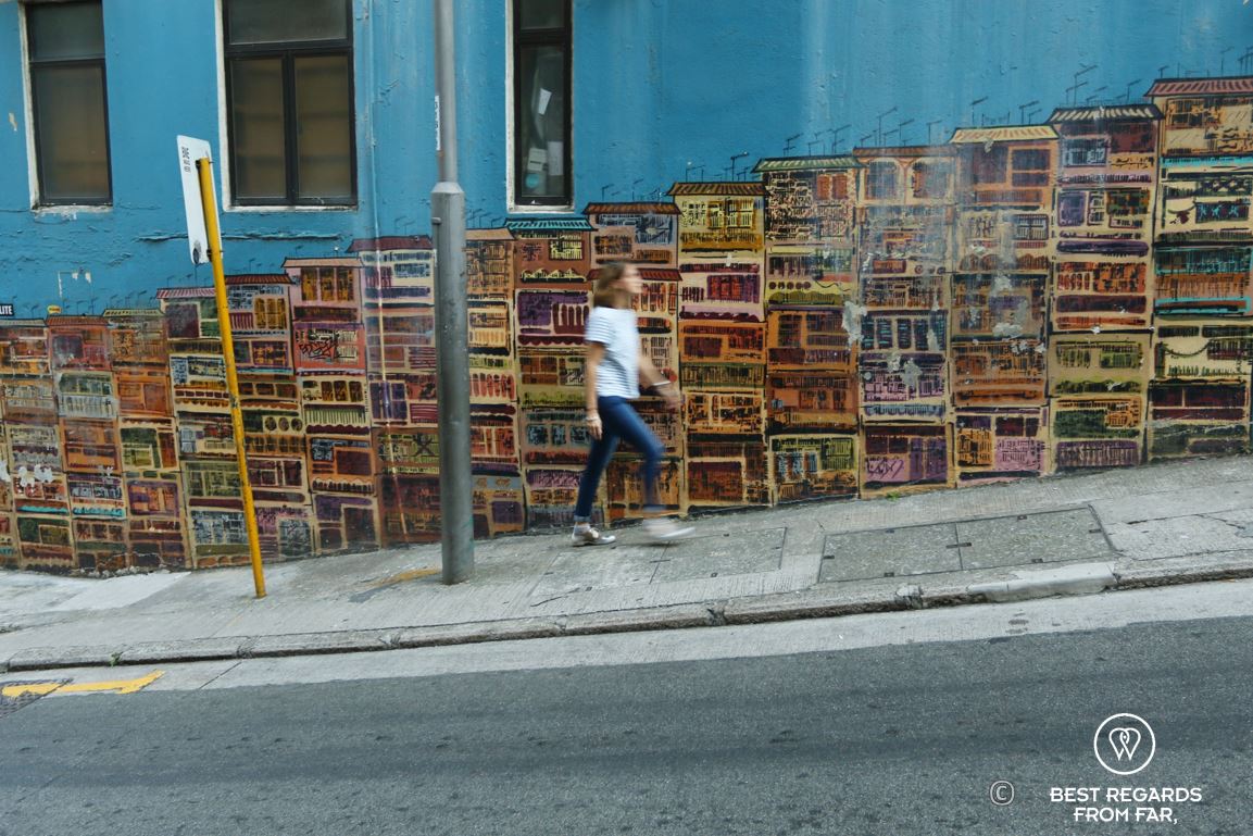 Fast-paced pedestrian walking in front of a mural street art showing buildings on Hong Kong Island