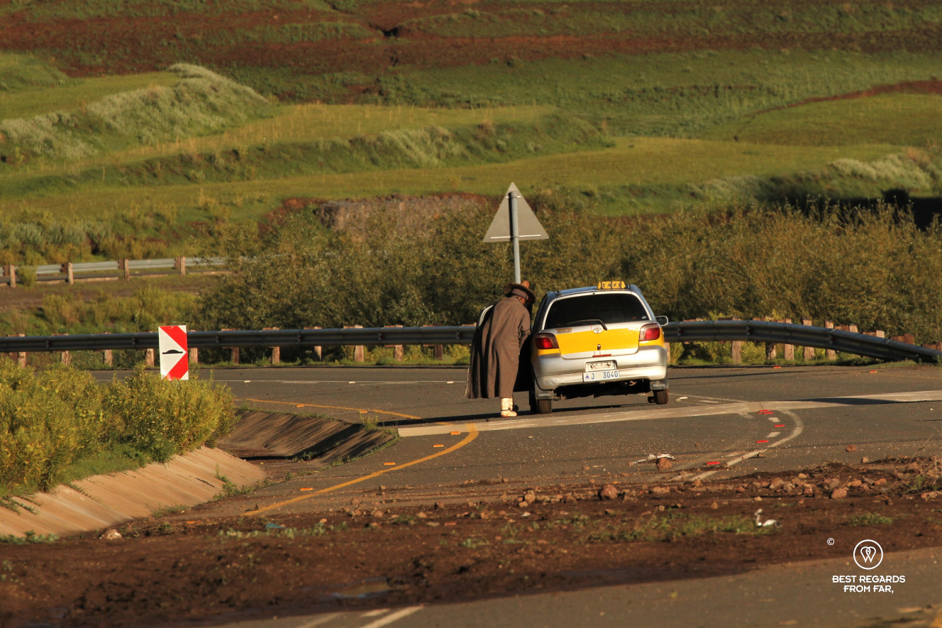 Shepherd in traditional Basotho clothes hopping in a taxi on a half washed away brand new road