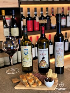 Three bottles of wine and a wine glass with red wine and some Italian bites
