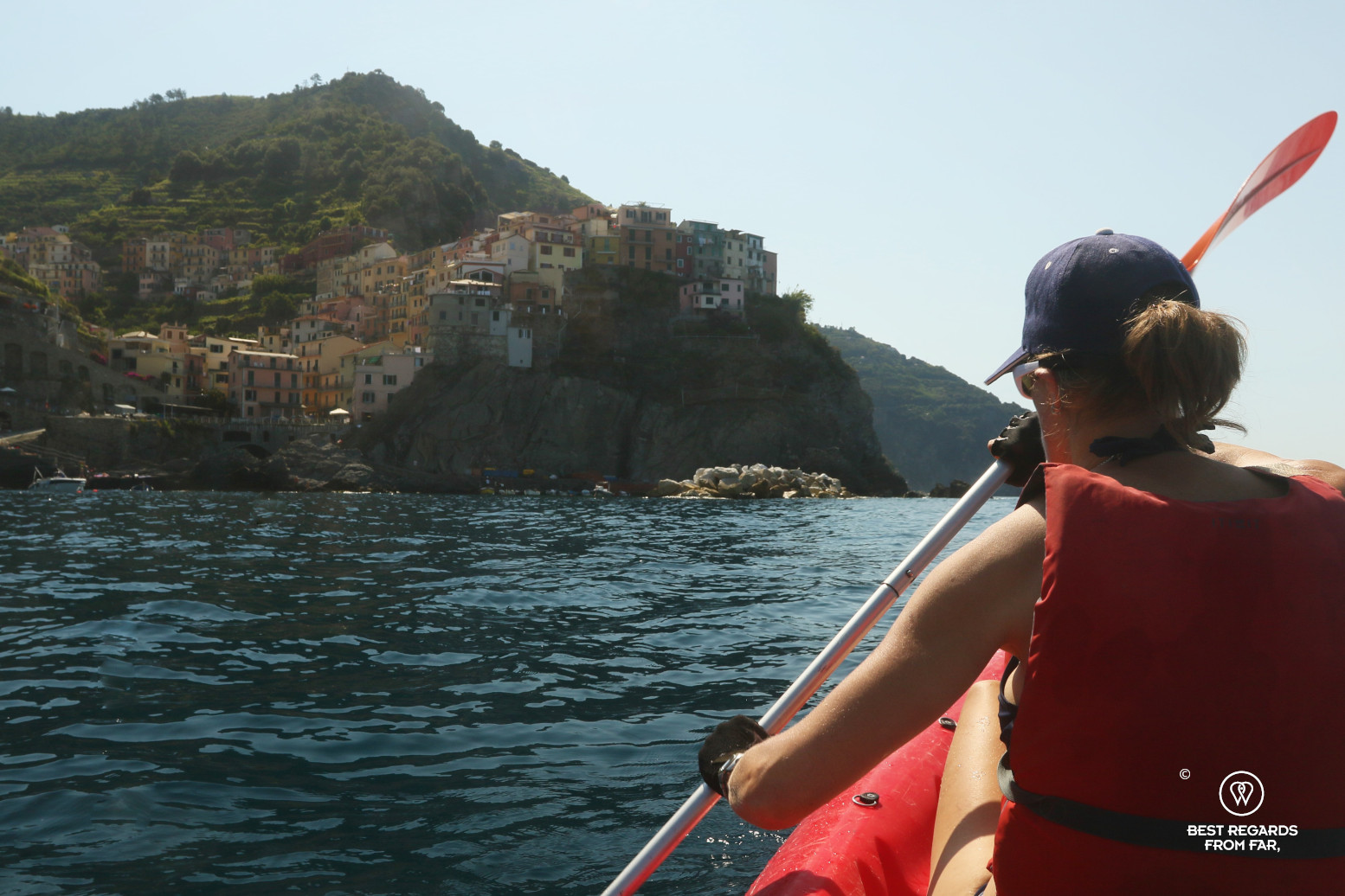 Woman kayaking on the sea by a village built on a cliff