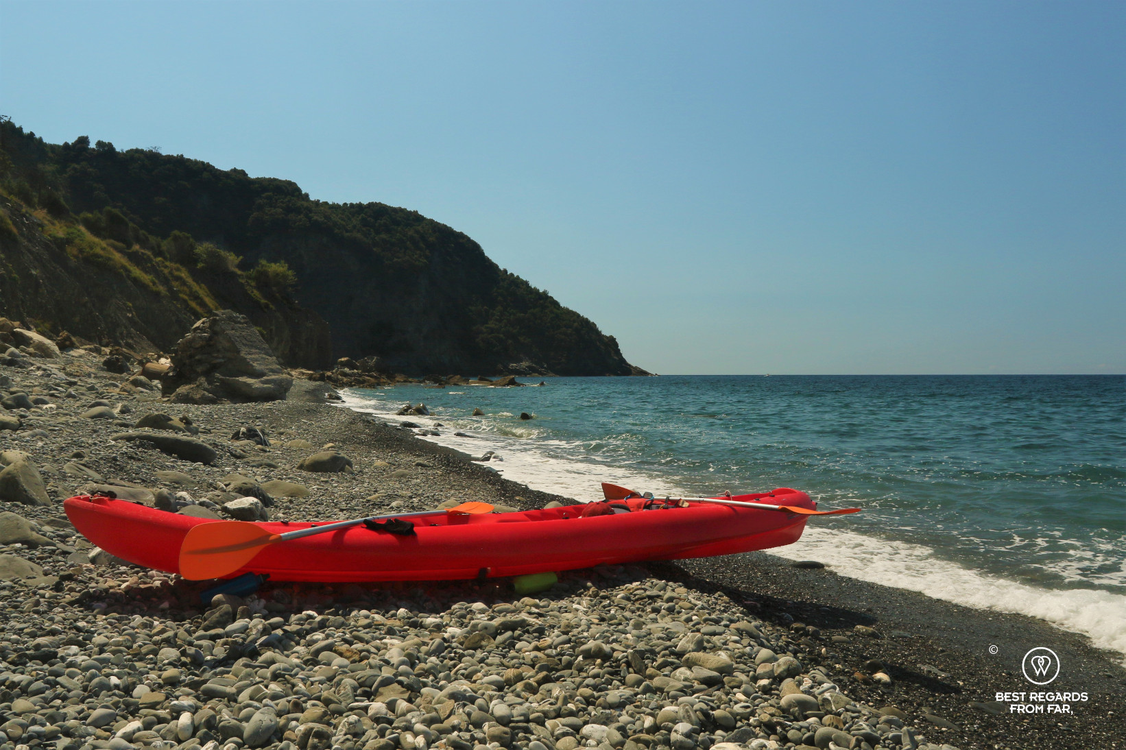 Red kayak on a rocky beack, the sea and blue skies, no people