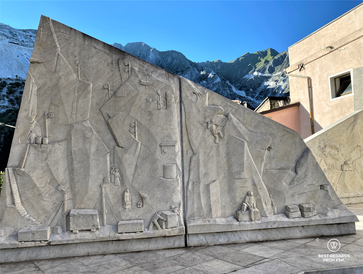 White marble statue of marble workers with the Carrara quarries in the background, Italy