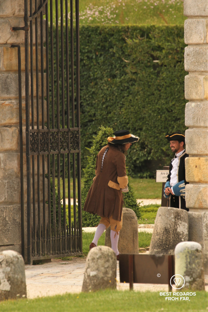 Two men smiling at each other in époque costumes in the gardens of the castle of Vaux le Vicomte, France.