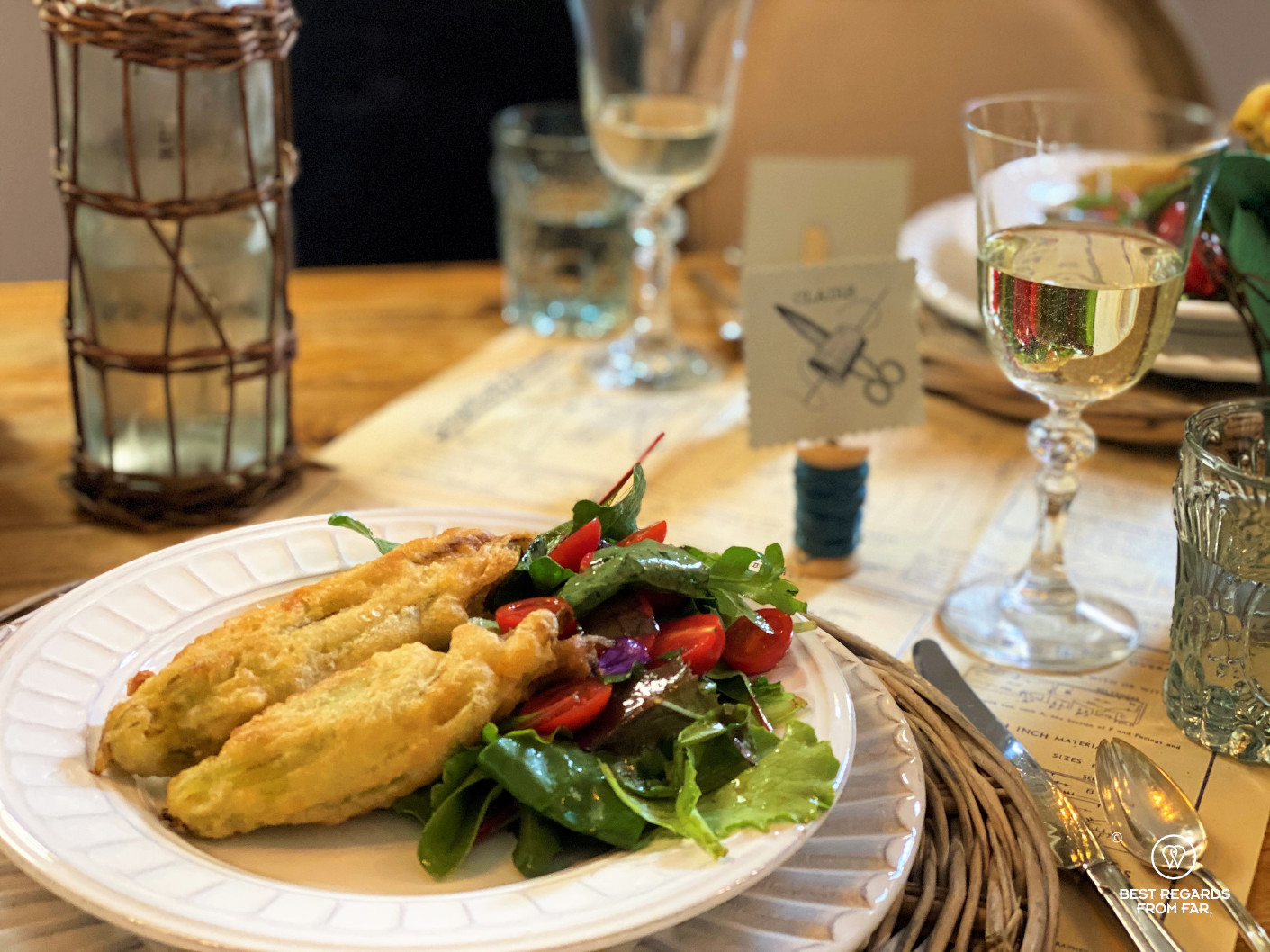 Fried zucchini flowers and salad served on a white plate with white wine