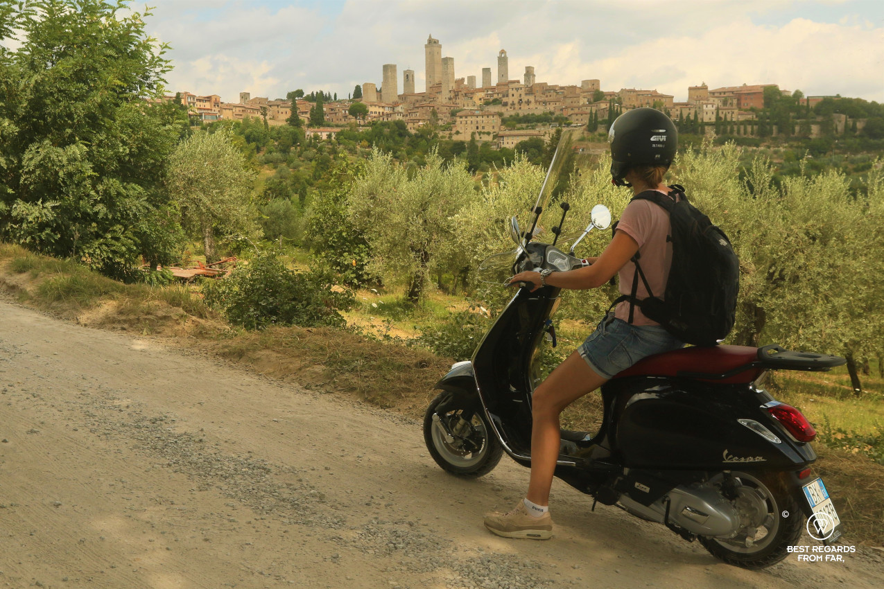 Riding a Vespa scooter with the towers of San Gimignano in the background, Tuscany, Italy
