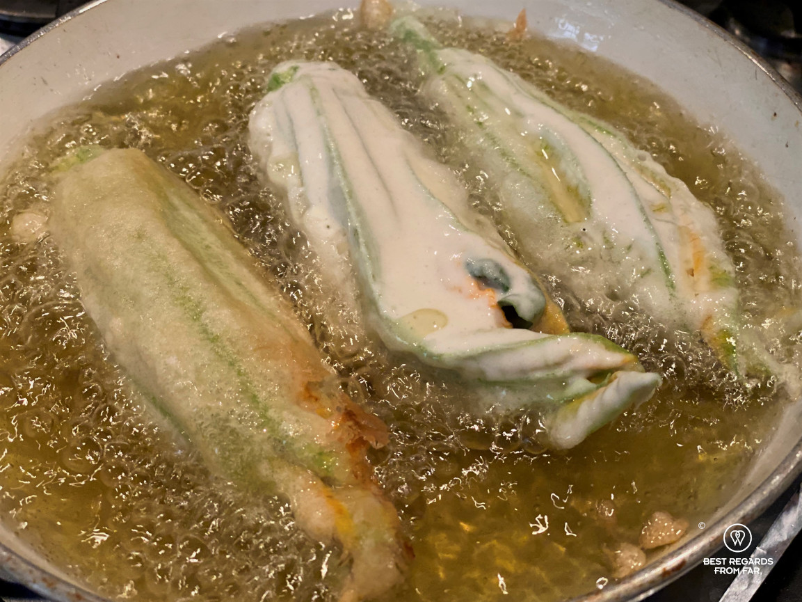 Three zucchini flowers being fried in a pan.