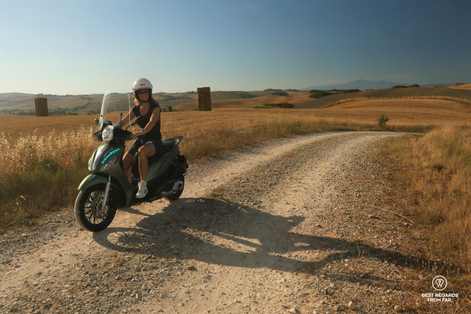 Woman driving a schooter in the golden hills at sunrise in Tuscany, Italy