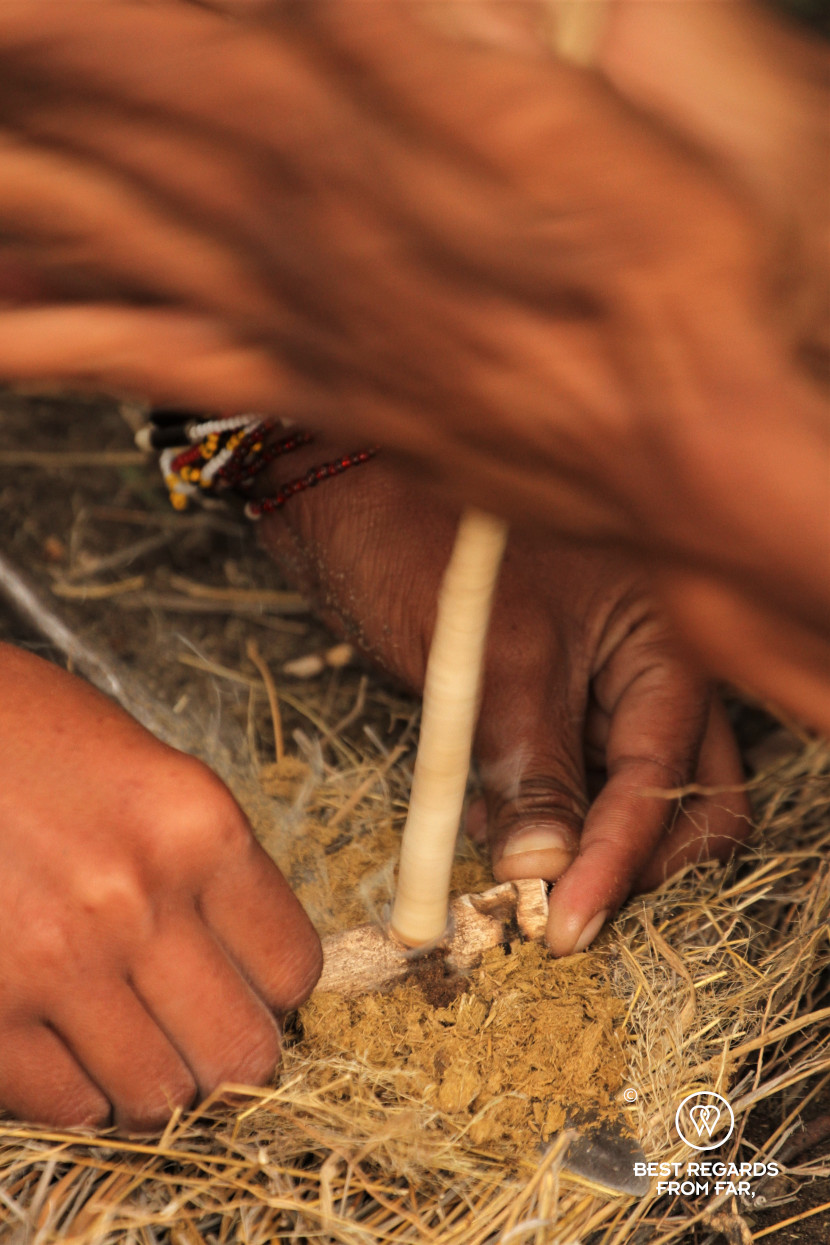San men making a fire by quickly rotating a dry stick on dry residues, Botswana.