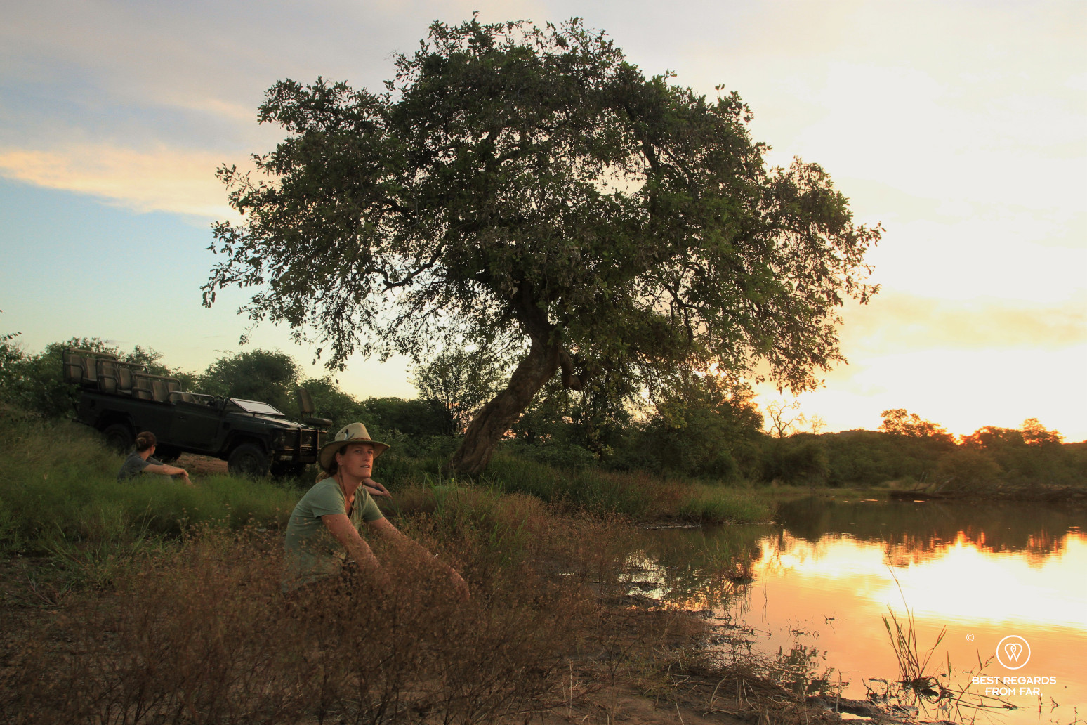 Safari-goer seated by a pond for sunset in the African bush