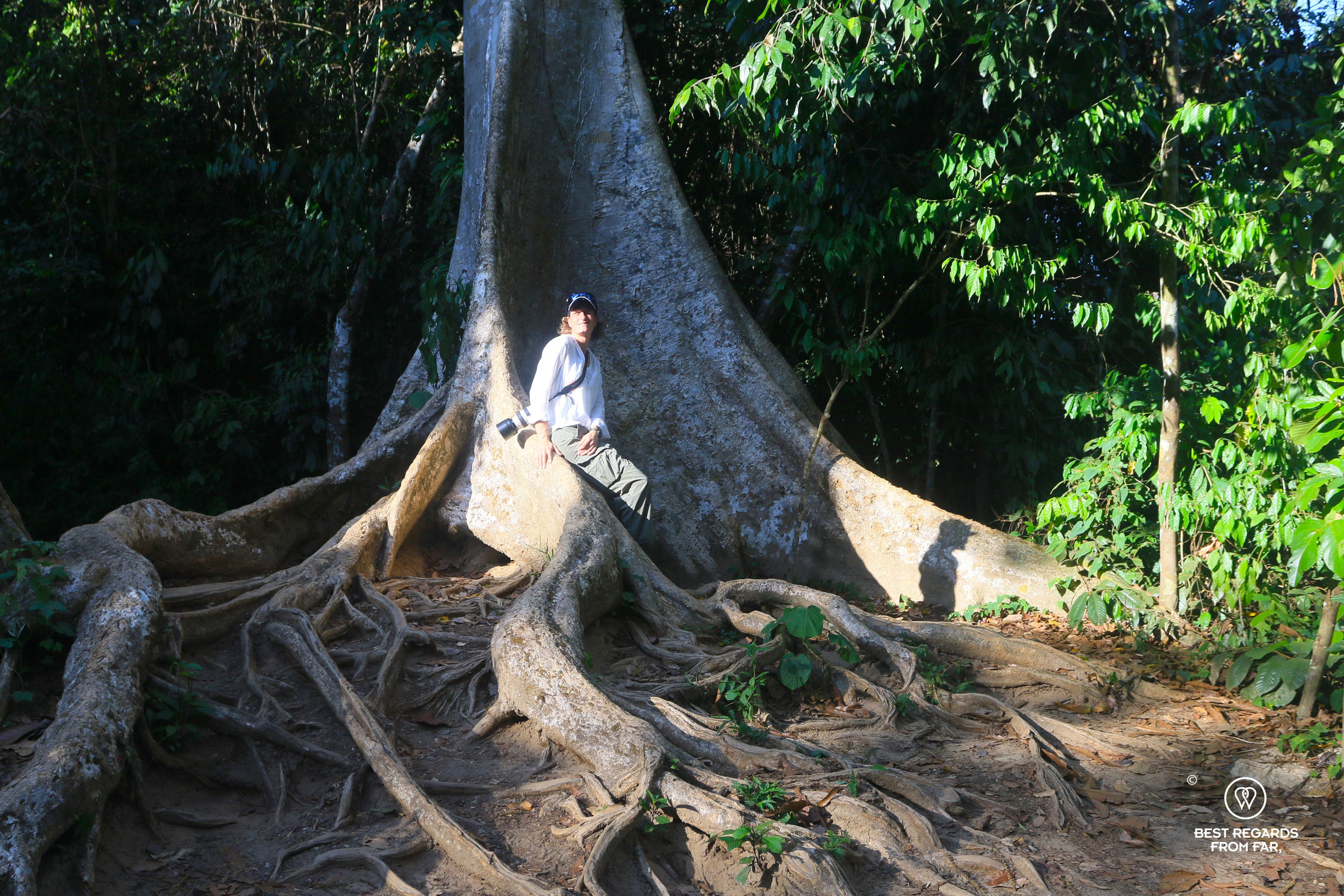Photographer Marcella van Alphen posing on a large tree root in the rainforest of Malaysia.