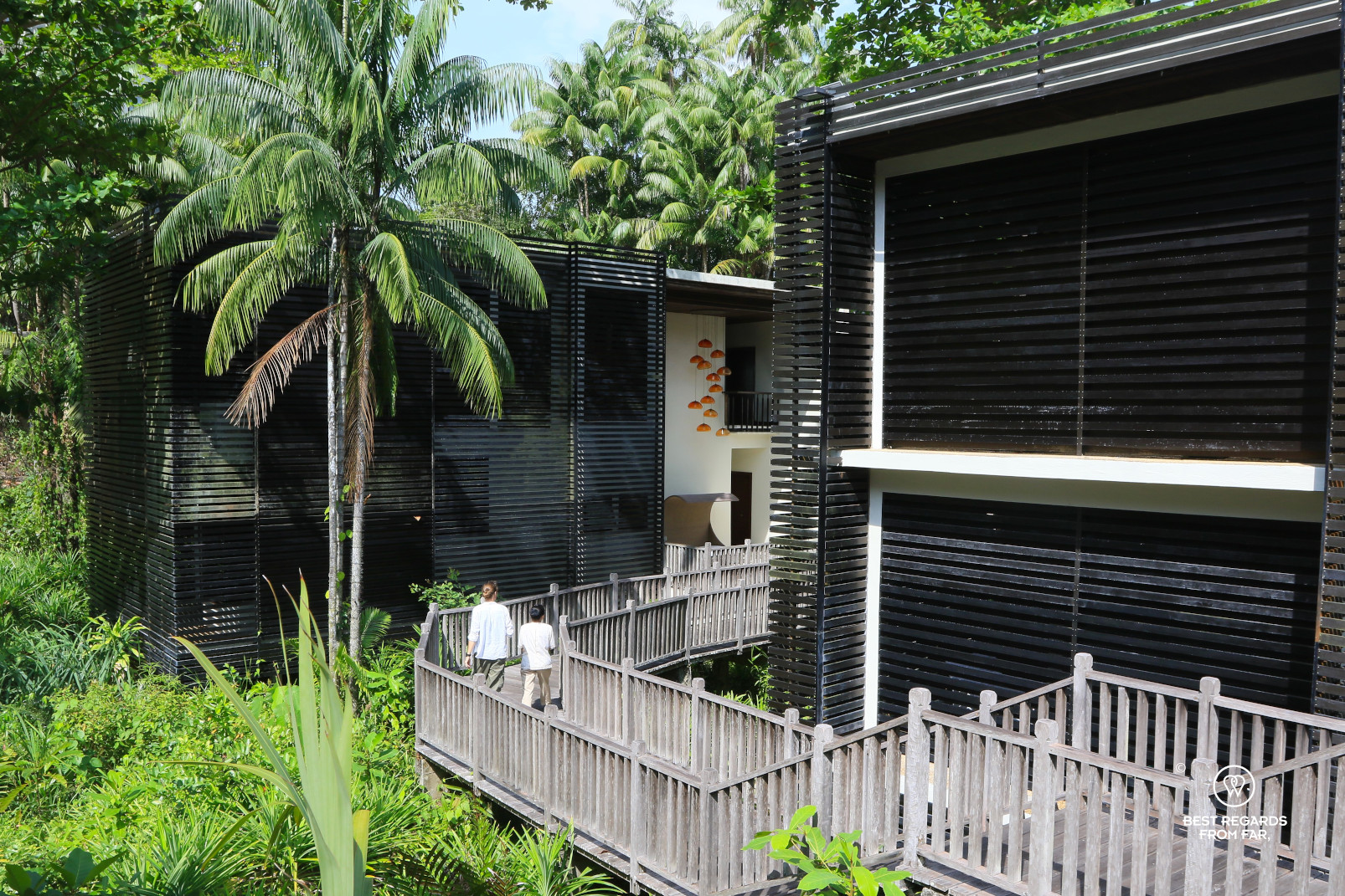 Guest and masseuse walking on a boardwalk of the Spa Village in the jungle of Gaya Island, Borneo.
