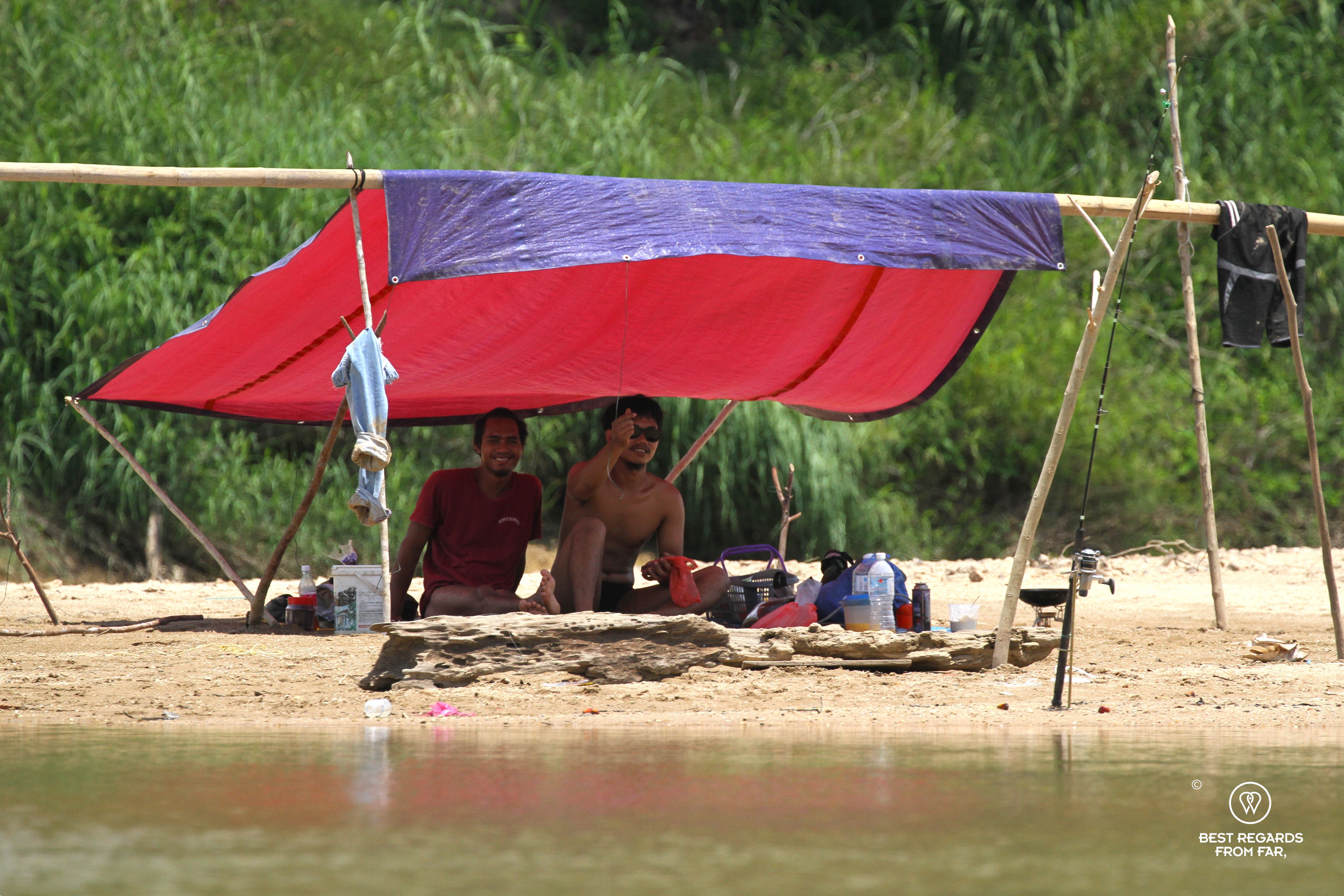 Two local fisherman waving from underneath a self-fabricated shelter along the Tembeling River.